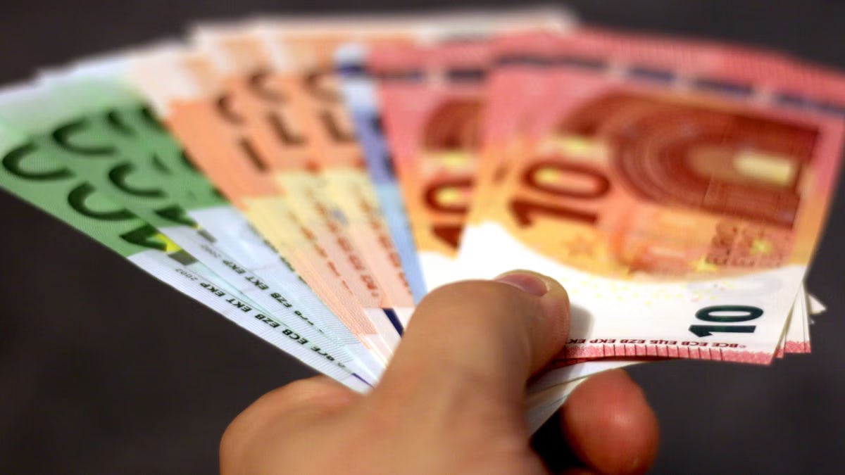 A close-up shot of a hand holding a fan of euro banknotes, symbolizing wealth and currency exchange.